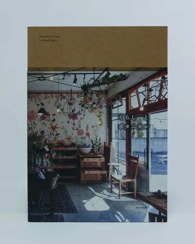 書籍『くらし と ボタニカル』の表紙。花の壁画と植物に囲まれた明るい室内の写真